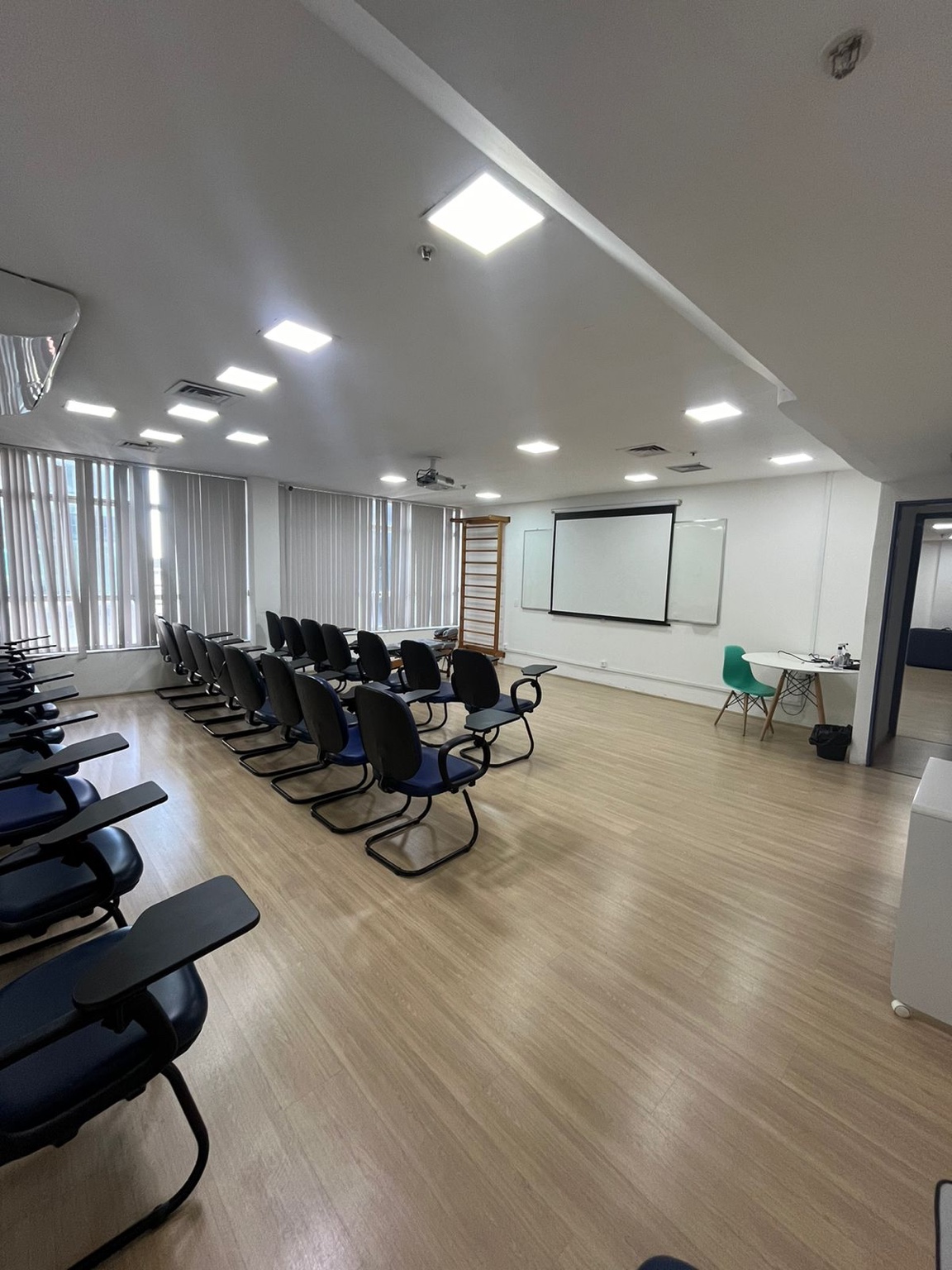 Auditório 2 com cadeiras com prancheta, tela de projeção, quadro branco e área frontal livre