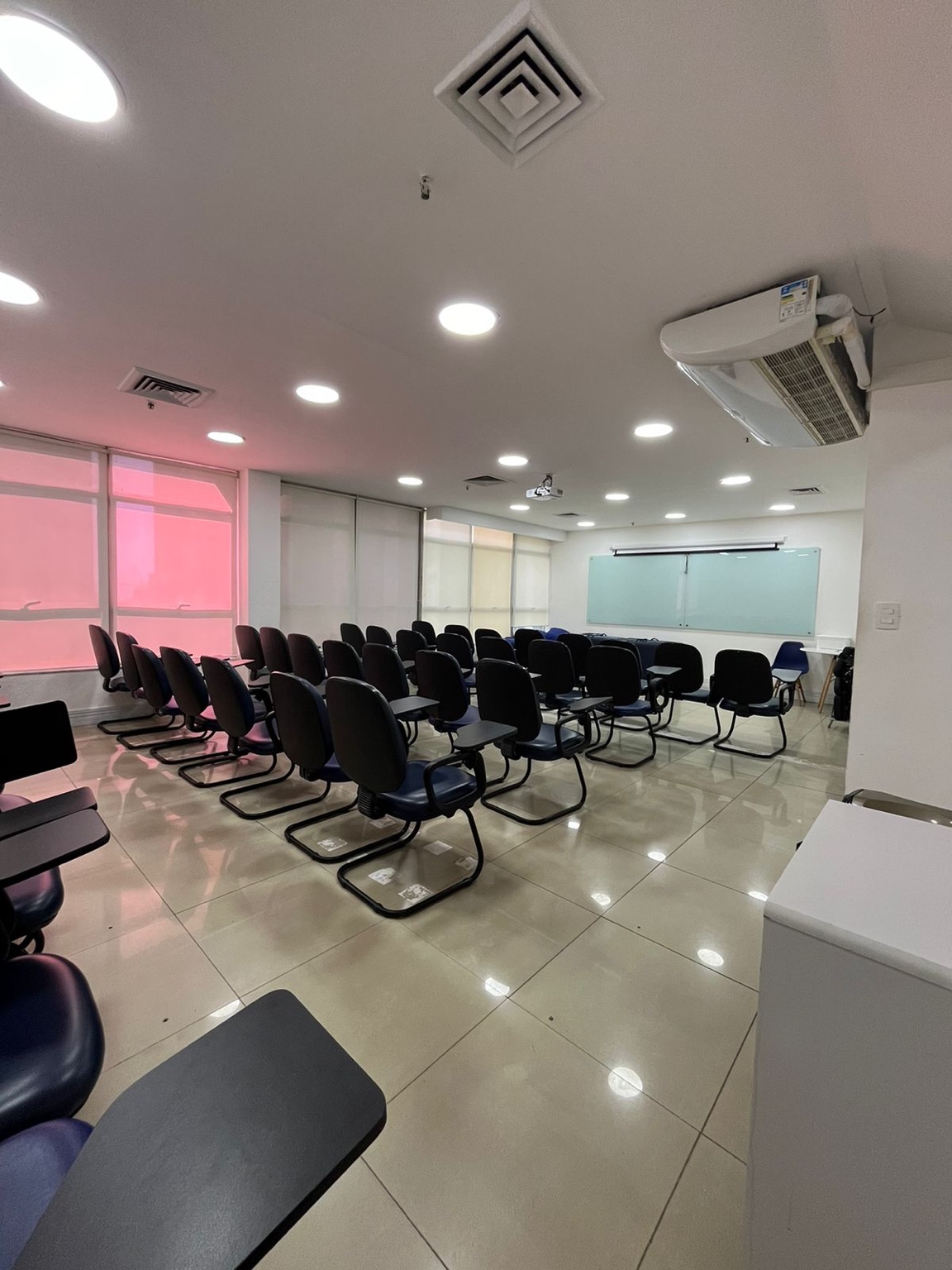 Auditório 3 da InterFISIO com cadeiras com prancheta, quadro de vidro e projetor no teto